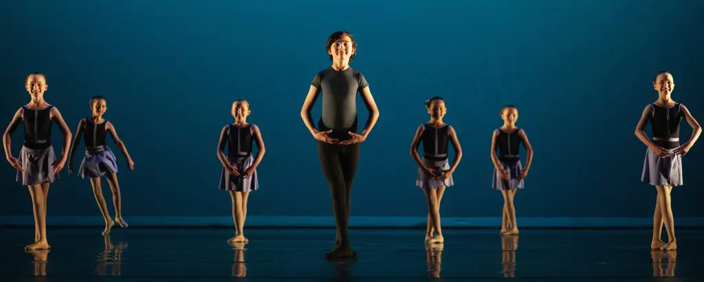 Promotional image of a boy dancing on stage, surrounded by an ensemble of girls.